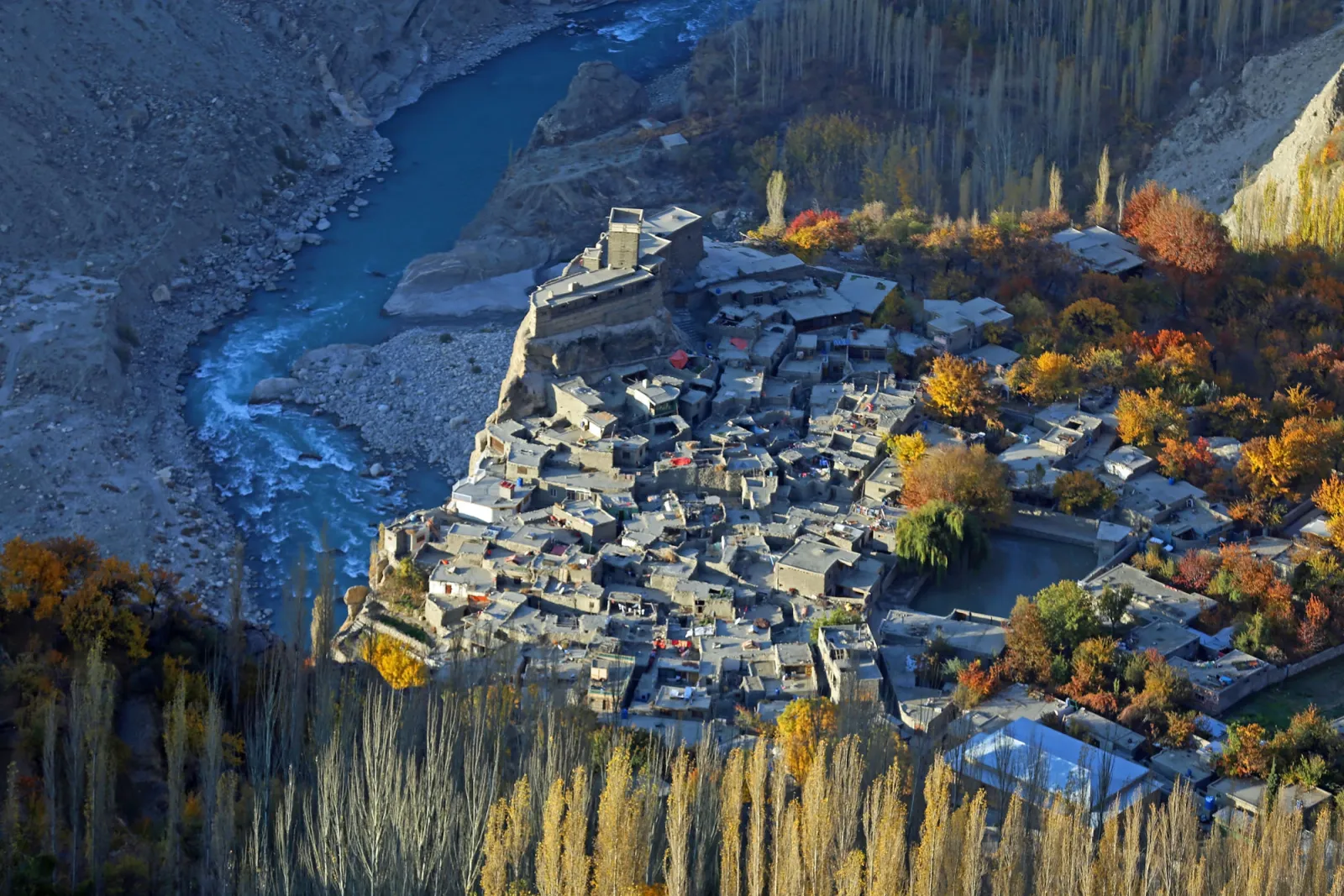 Il Forte Altit arroccato su uno sperone roccioso sopra il fiume Hunza turchese, con l'antico villaggio e i pioppi autunnali in basso