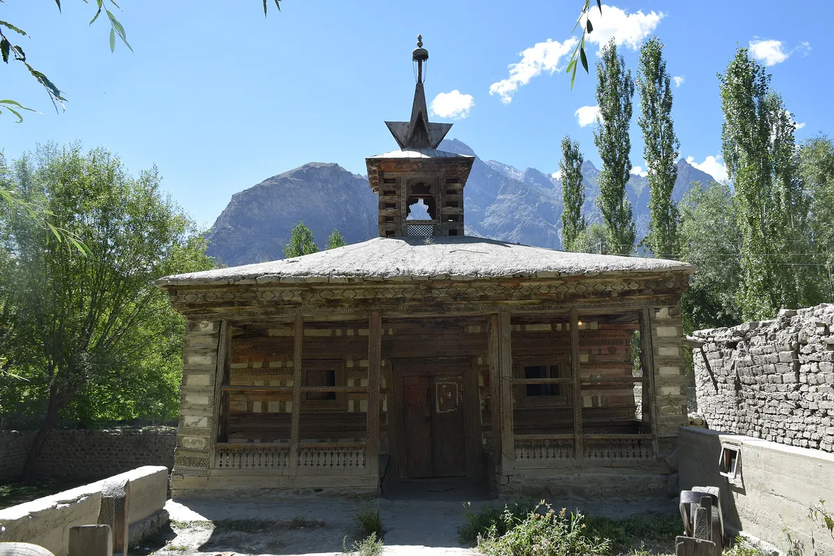 The small wooden Amburik Mosque in Shigar valley near Skardu, with a tiered timber spire, poplars and mountains behind