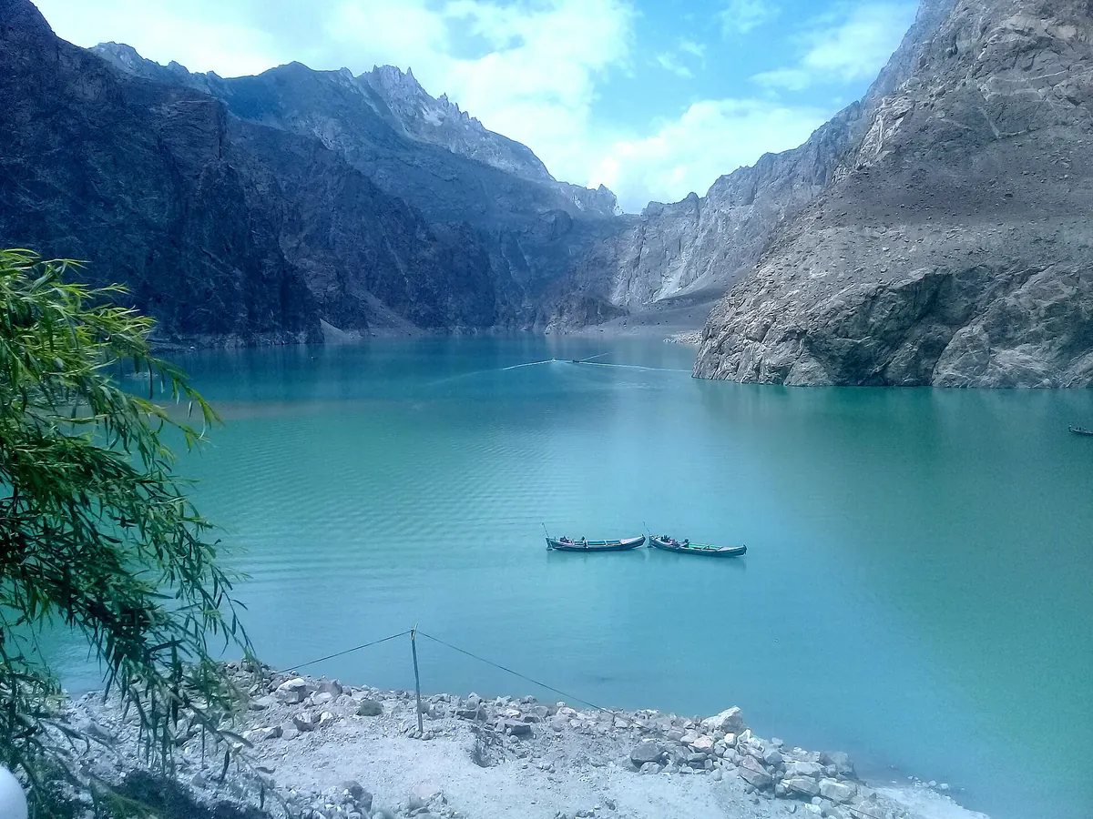 Der türkisfarbene Attabad-See zwischen steilen Felswänden im oberen Hunza, zwei Boote auf dem Wasser, Gilgit-Baltistan, Pakistan