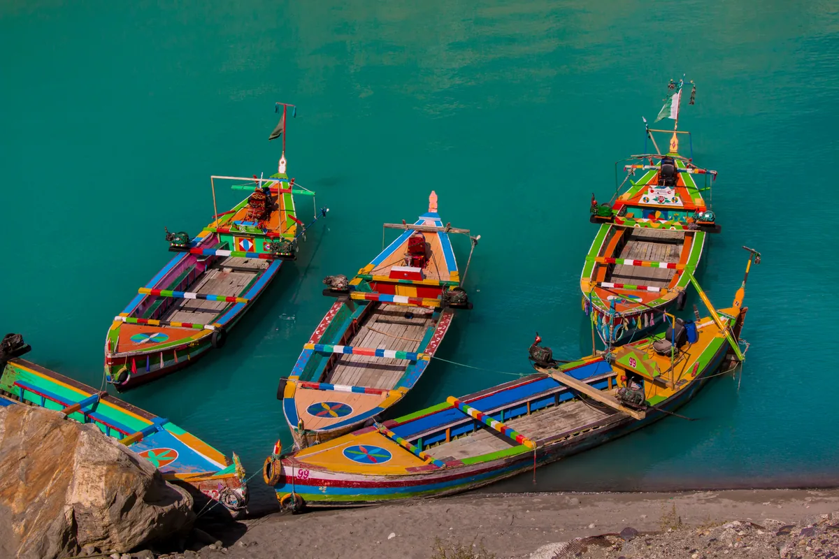 Bemalte Holzboote am türkisfarbenen Wasser des Attabad-Sees in Hunza, bereit für Seefahrten