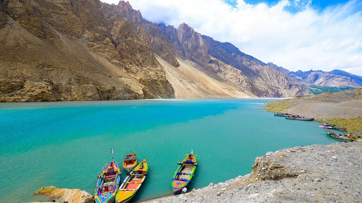 Barche dipinte a colori vivaci ormeggiate sull'acqua turchese del lago Attabad, alta Hunza, sotto le ripide falesie del Karakorum