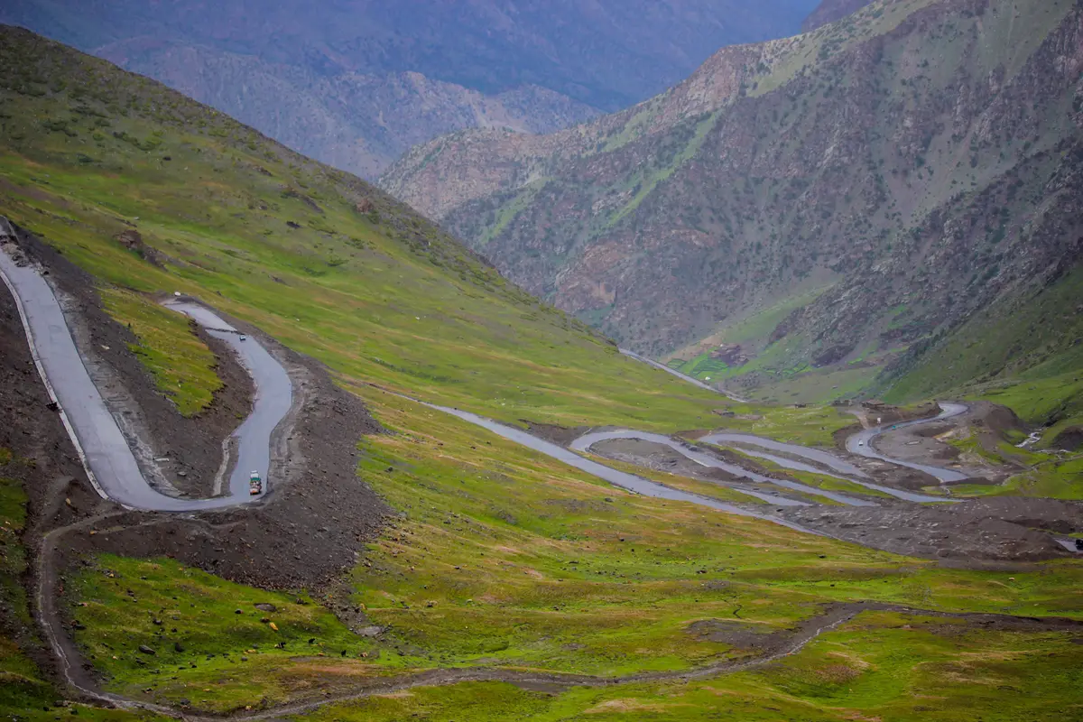 Strada a tornanti che sale tra i verdi pascoli alpini verso il Babusar Pass, valle di Kaghan, Pakistan settentrionale