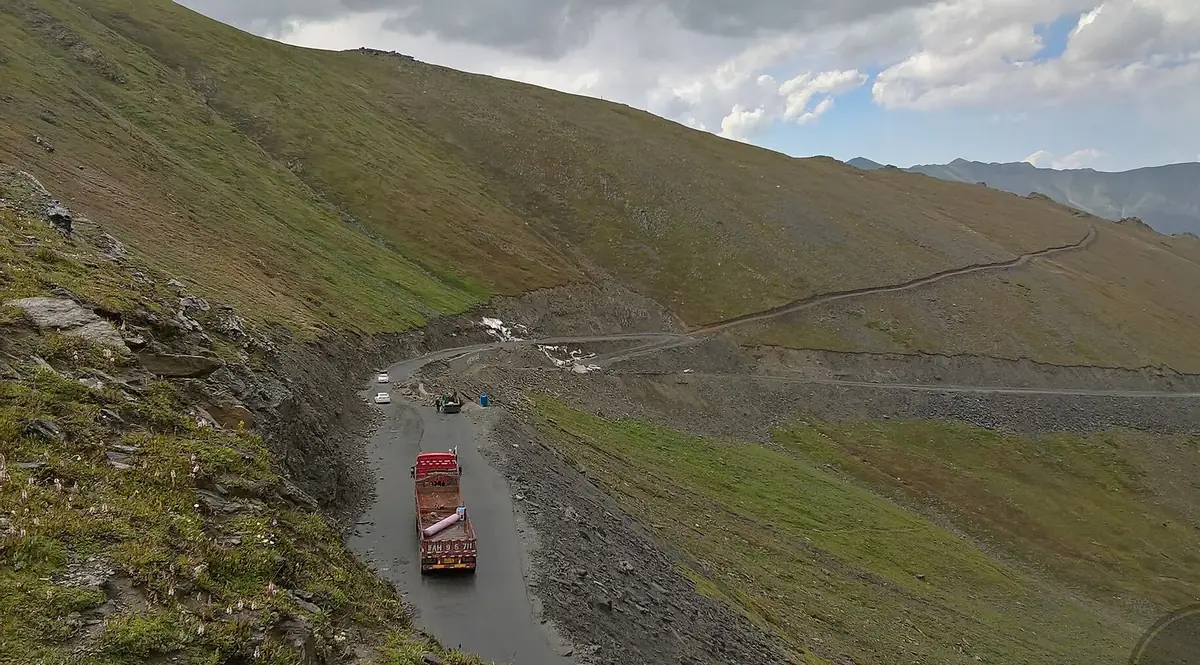 A colourful truck and cars on the steep switchbacks of the Babusar Pass road cut into a green mountainside, Kaghan, Pakistan