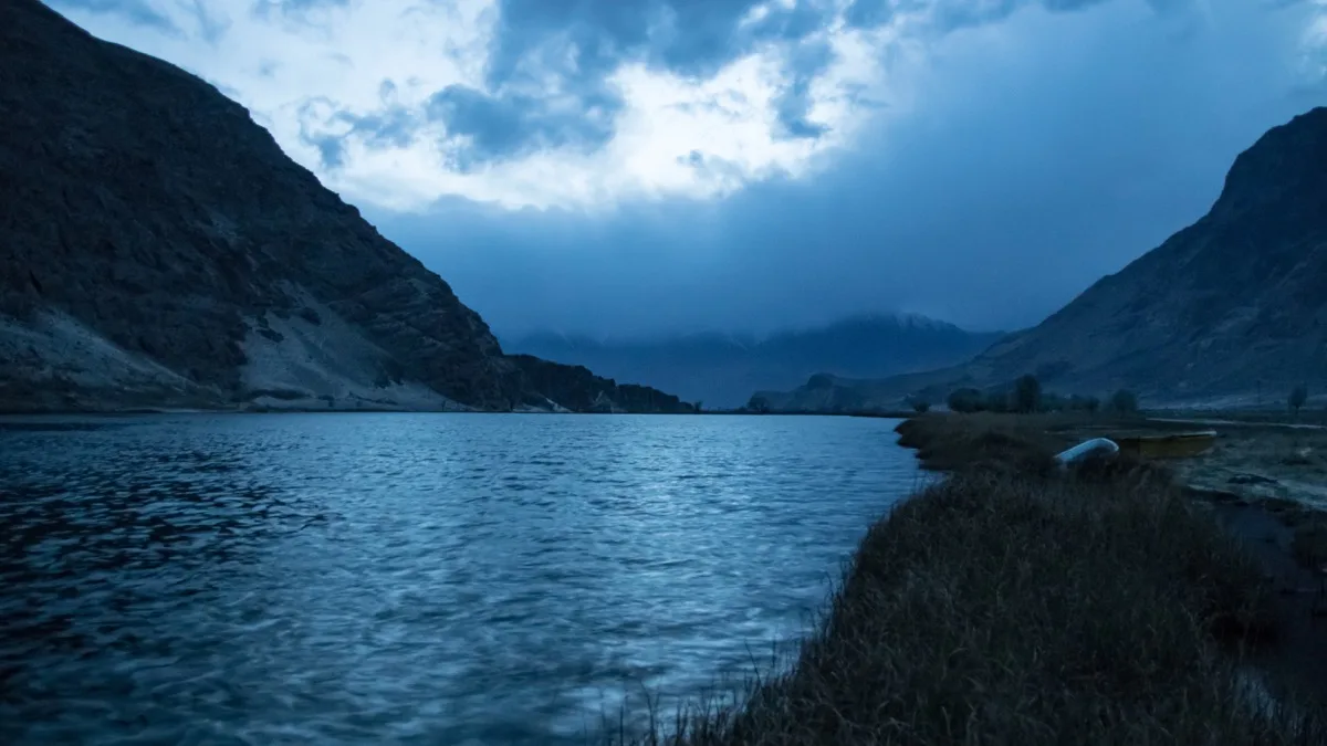 A small wooden boat pulled up on the grassy bank of Blind Lake (Zharba Tso) under storm cloud at dusk, Shigar valley near Skardu, Pakistan