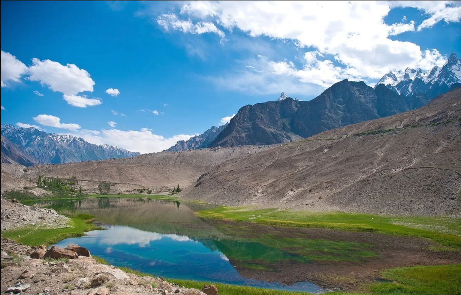 Le acque turchesi e immobili del lago Borith circondate da prati verdi e brulli pendii di Gojal, alta Hunza