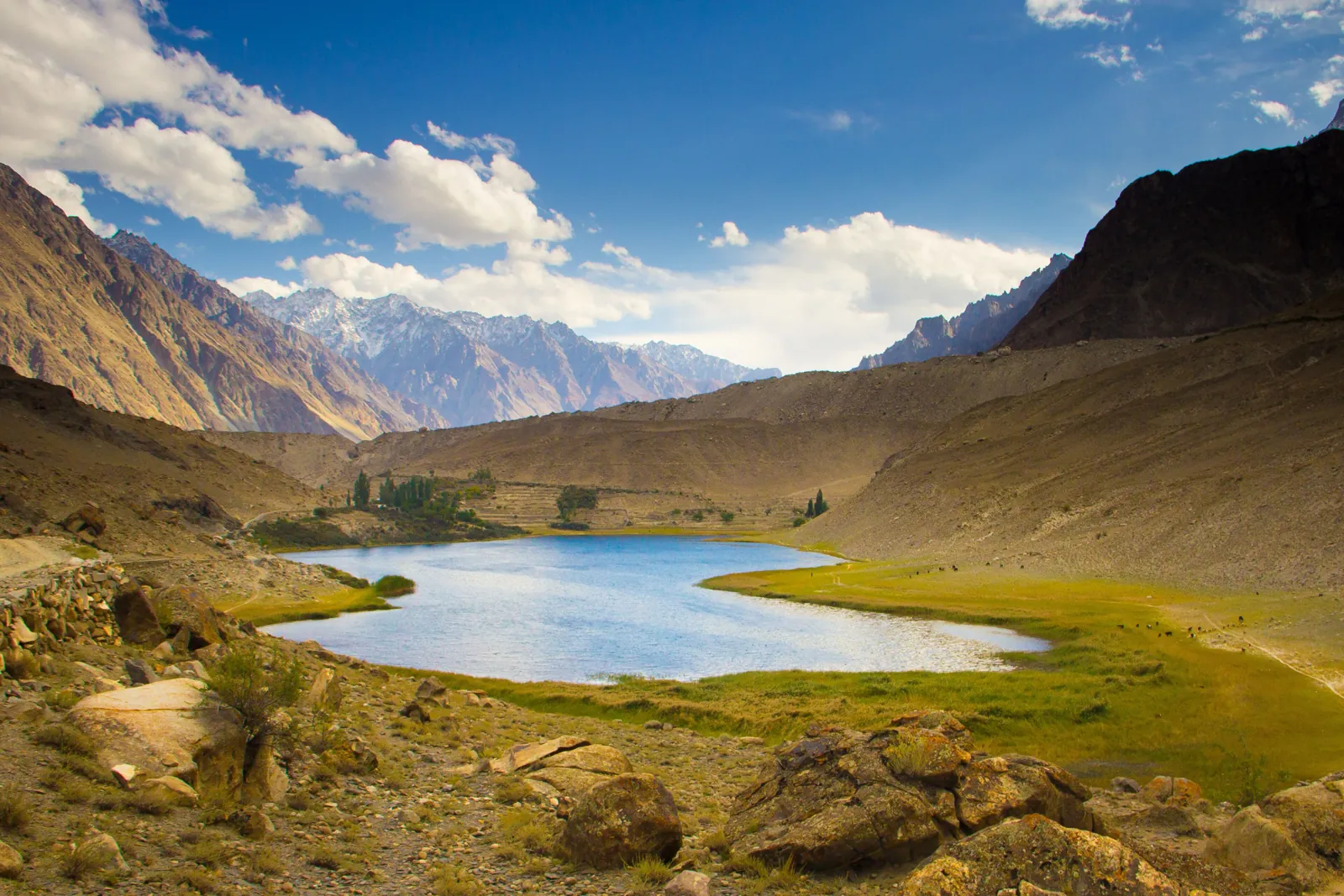 Borith Lake in a green hollow above Gulmit in upper Hunza, with brown hills and snow peaks behind