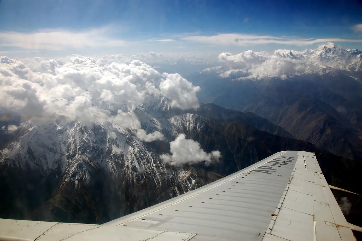 Wing-seat view from a flight to Skardu over snowy Karakoram ridges and clouds, high above the mountains of Baltistan