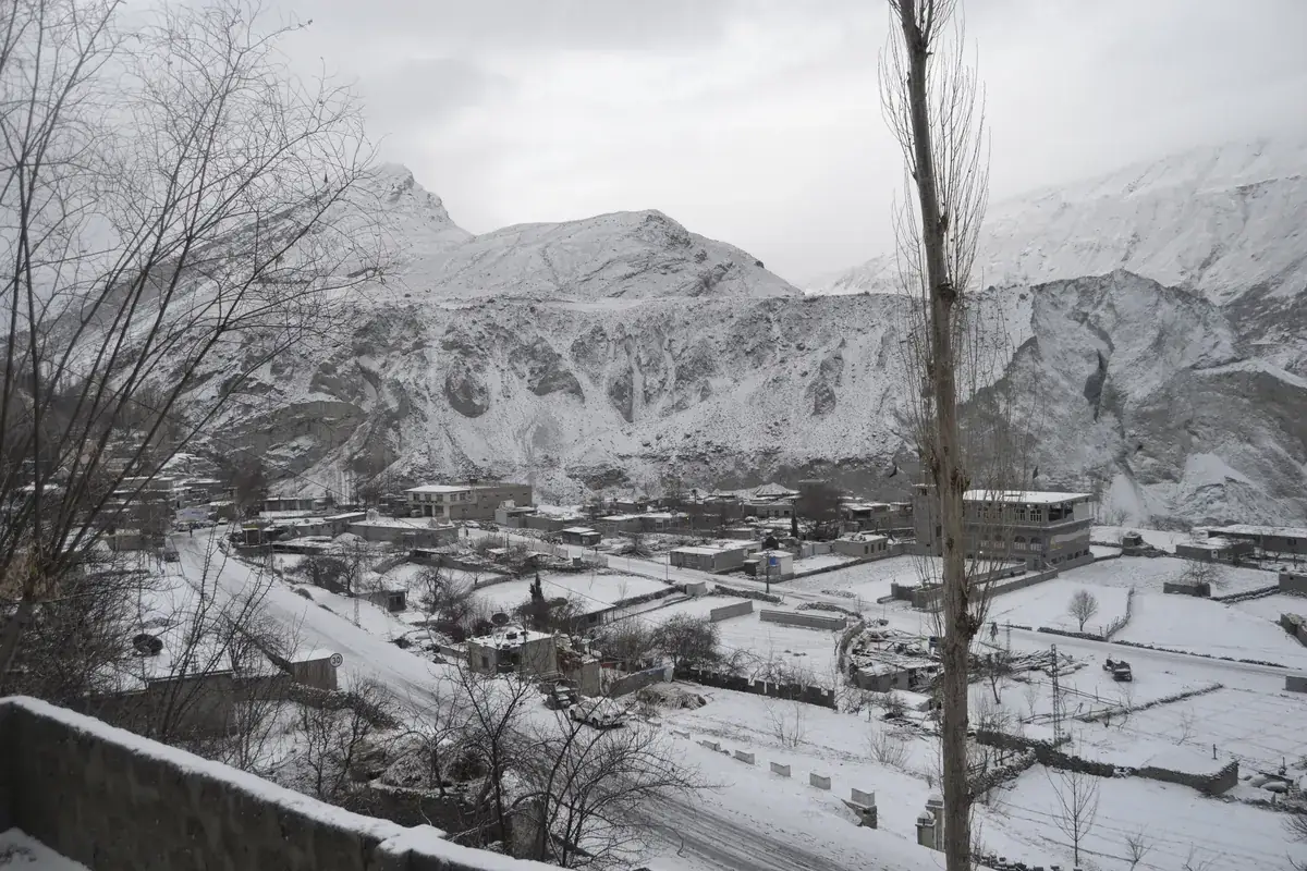 Snow covering the flat roofs and fields of Ganish village in Hunza in January, under grey winter cloud and white mountains