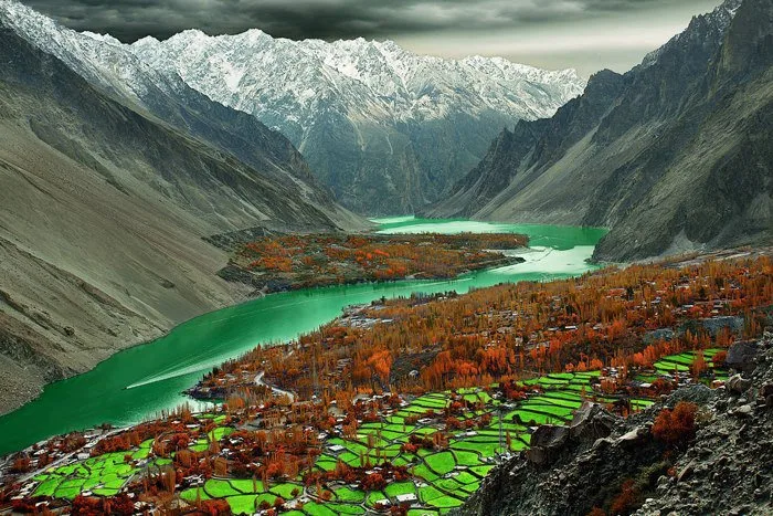 I campi terrazzati verdi e i pioppi autunnali del villaggio di Gulmit a Gojal, alta Hunza, sopra le acque smeraldo della valle