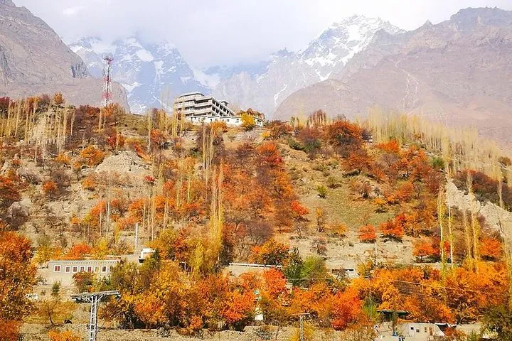 Orange and red autumn trees on a hillside village below snow-dusted peaks in the Hunza-Nagar area, Gilgit-Baltistan