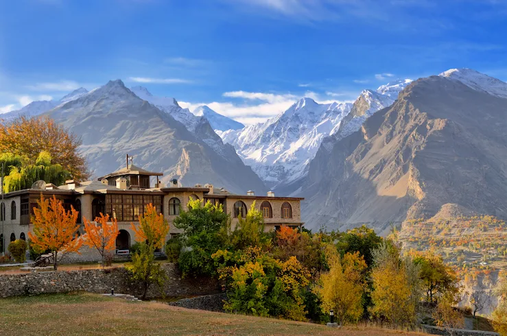 Colori autunnali attorno a un lodge tradizionale in pietra nella valle di Hunza, con le cime innevate del Karakorum sullo sfondo, Gilgit-Baltistan, Pakistan