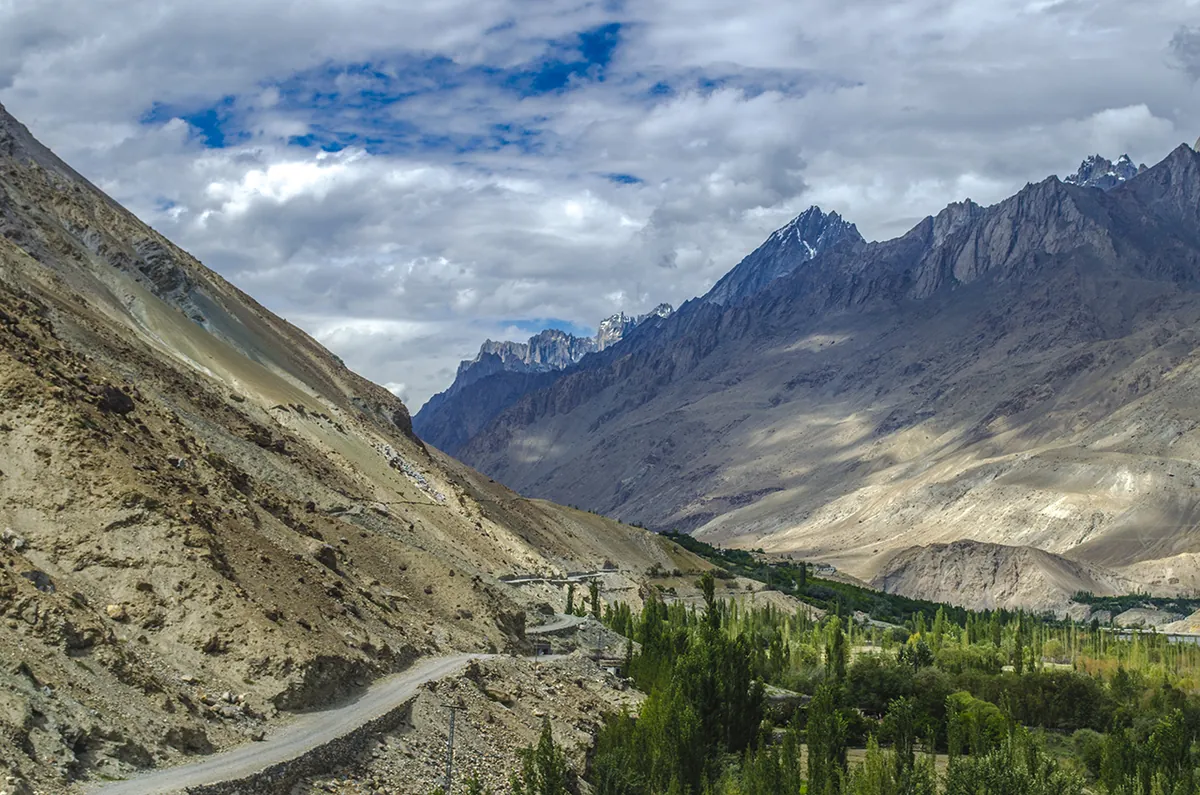 The road into Hushe Valley beyond Khaplu, winding between dry slopes towards jagged Karakoram peaks under a cloudy sky