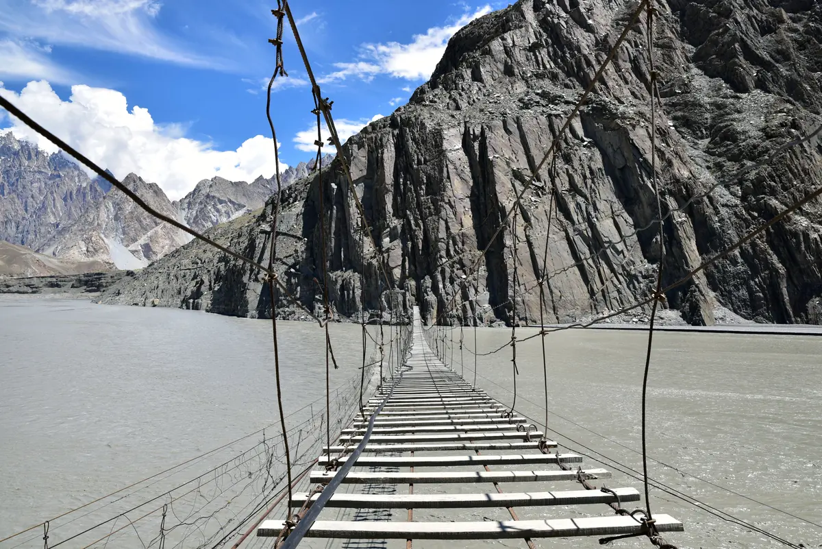 Blick über das lückenhafte Plankendeck der Hussaini-Hängebrücke über den Hunza-Fluss bei Passu
