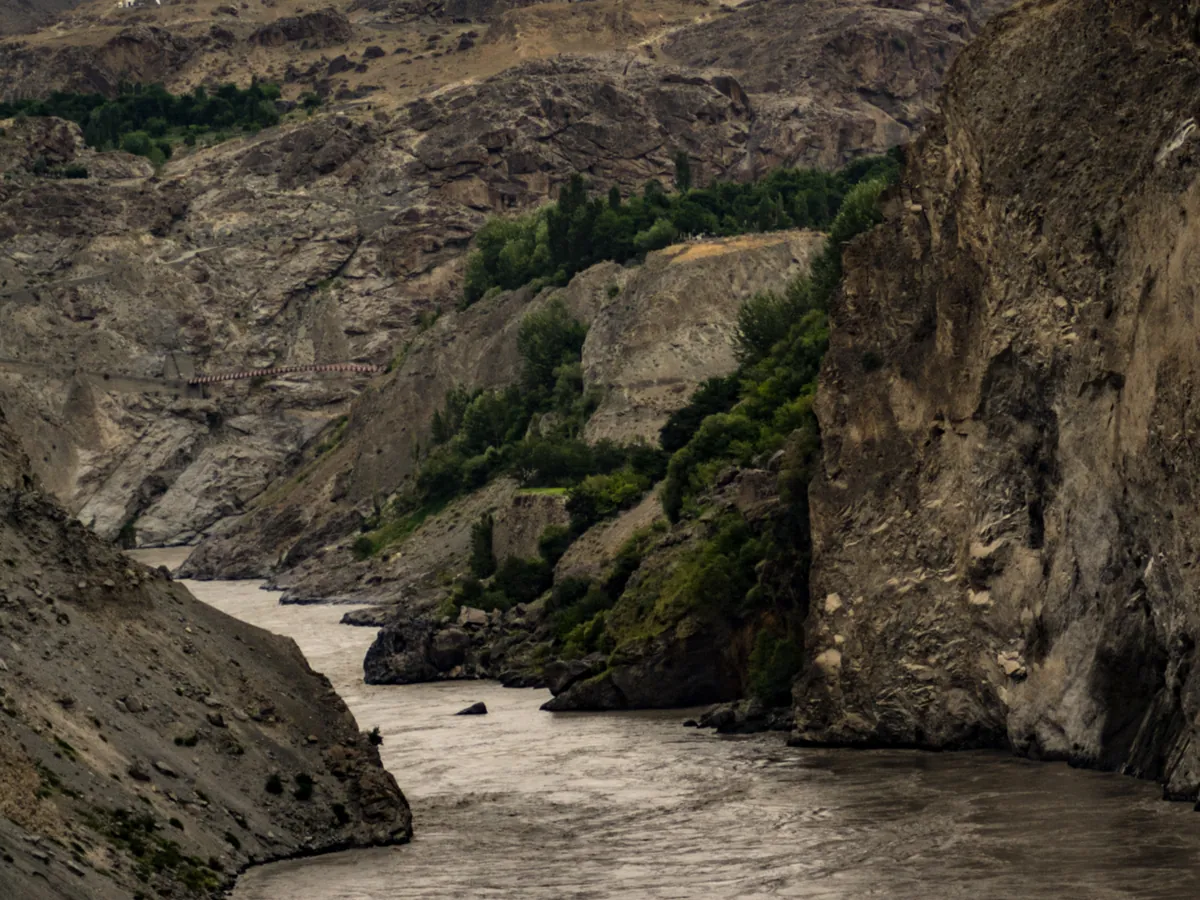 The brown Indus River running through a steep rock gorge with green trees on the slopes, seen from the Gilgit-Skardu road in Gilgit-Baltistan, Pakistan