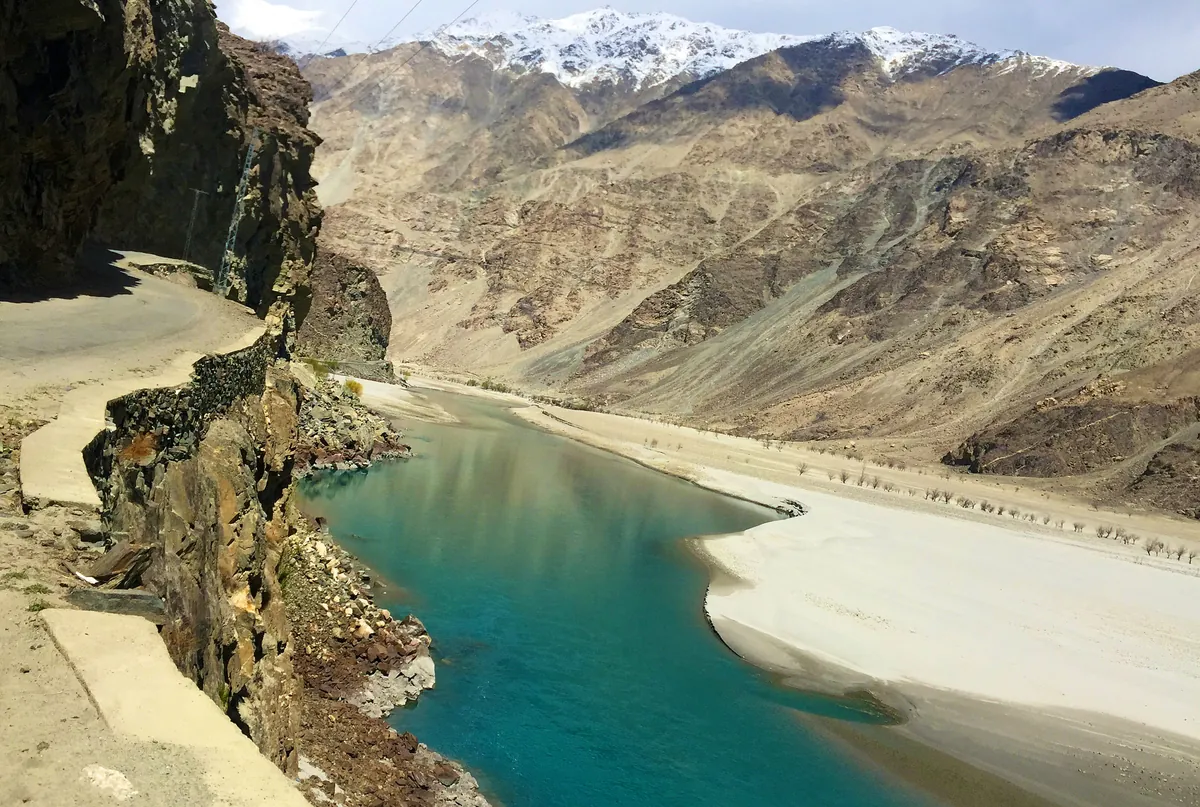 The turquoise Indus River below the Gilgit to Skardu road, cut into the rock wall of the gorge, with snow-dusted peaks above