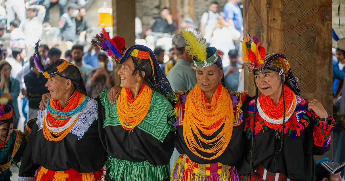 Donne kalash in abiti neri tradizionali, collane di perline arancioni e copricapi piumati alla festa Chilam Joshi, Chitral, Pakistan