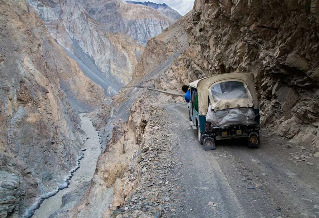 Jeep mit beladenem Dach auf der schmalen Piste an der Felskante über einer Flussschlucht auf dem Weg nach Shimshal, Gojal, oberes Hunza