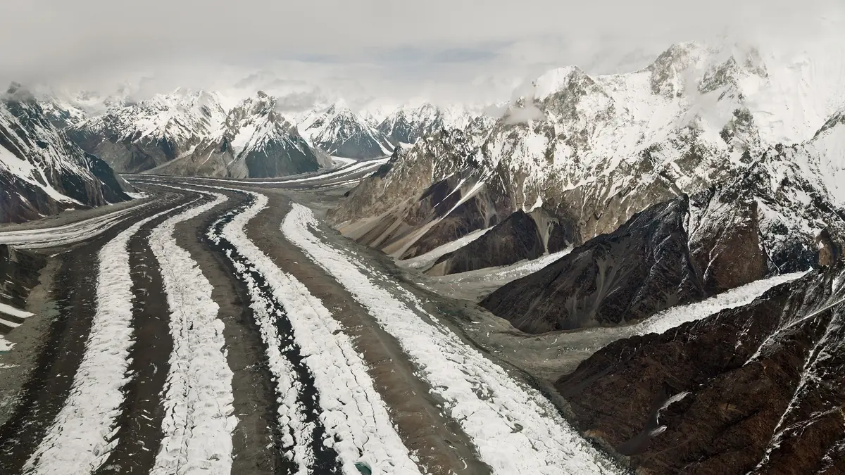 Aerial view of the dark medial moraine stripes running down the Baltoro Glacier between snow peaks in the Karakoram, Pakistan