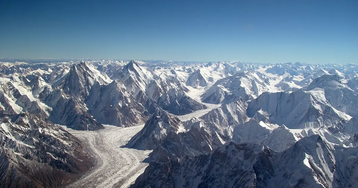 Aerial view over the Karakoram Range in Pakistan, a glacier winding between snow-covered peaks stretching to the horizon