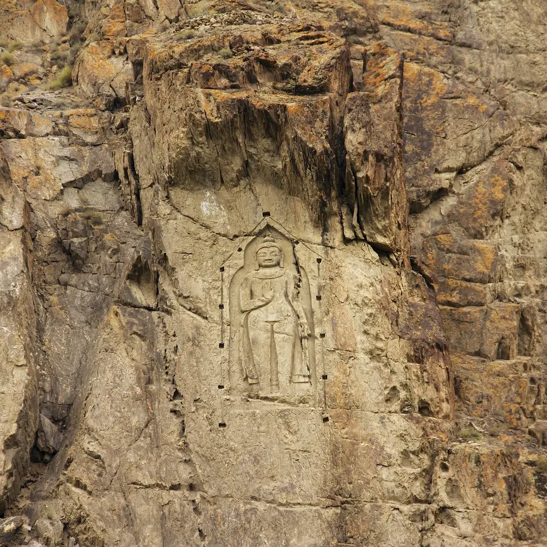 Close view of the Kargah Buddha relief, showing the robes, the raised hand and the square socket holes cut into the rock around the panel