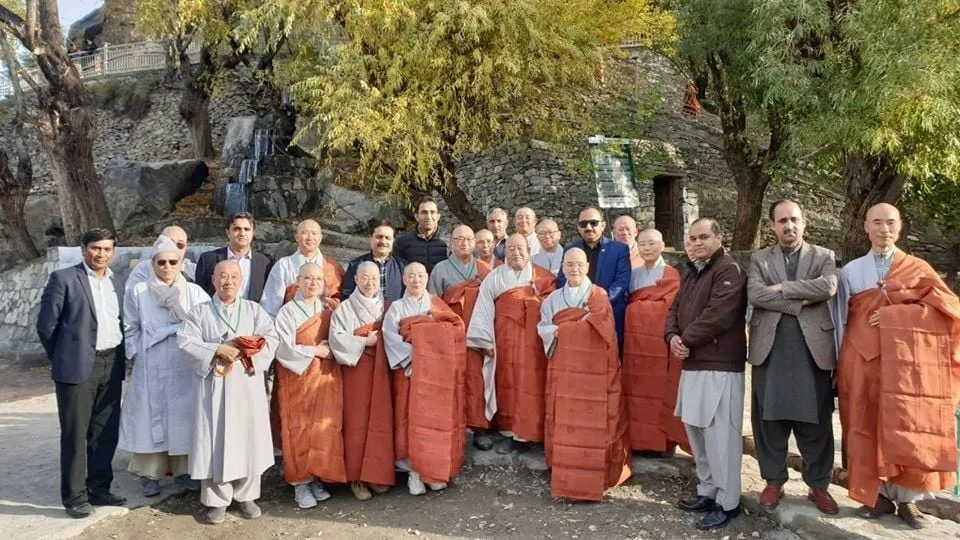 A Buddhist delegation of monks and officials photographed together at the foot of the Kargah Buddha cliff in Gilgit