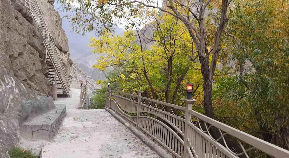 The paved walkway and steps running along the base of the cliff at Kargah, with railings and autumn trees