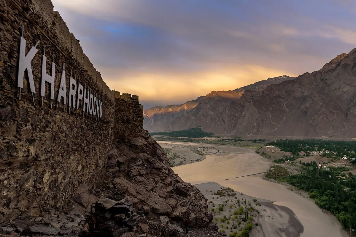 Kharpocho Fort's stone wall with its painted name, high above the Indus river valley at Skardu at sunset