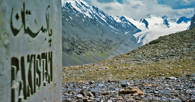 The Pakistan boundary pillar on the Mintaka Pass at 4,709 m, with slate scree in front and snow peaks and a glacier on the China side behind, upper Hunza, Pakistan
