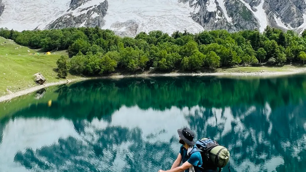A trekker on the shore of Kutwal Lake looking across the water to the snow and ice of Haramosh Peak, Gilgit-Baltistan