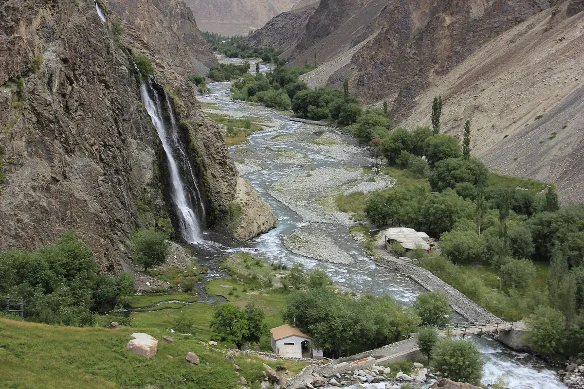 Manthokha Waterfall dropping down a rock face in Kharmang valley, with green fields and a river below