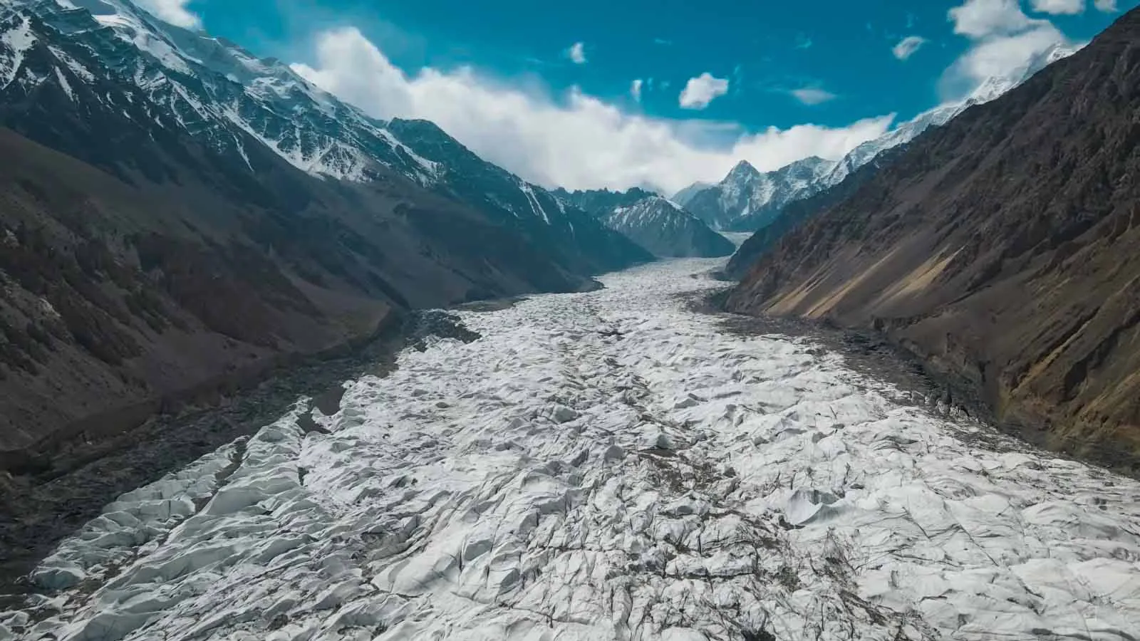 La bianca lingua fessurata del ghiacciaio di Passu che serpeggia lungo la valle tra le vette innevate, Gojal, alta Hunza