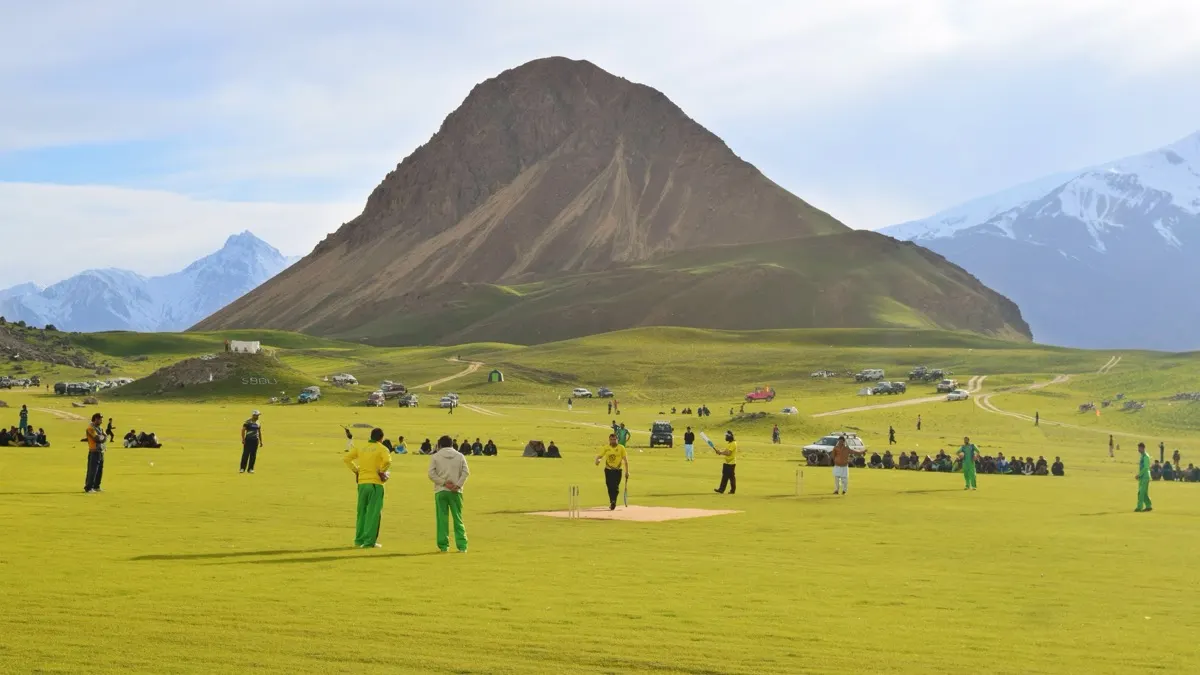 A sports match in progress on the grass at the Qaqlasht festival in Chitral, with spectators, tents and a conical peak behind, Pakistan