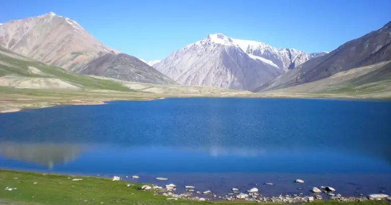 A glacial lake on the Shimshal Pamir with a snow peak above it and summer grazing grass along the shore, Gilgit-Baltistan