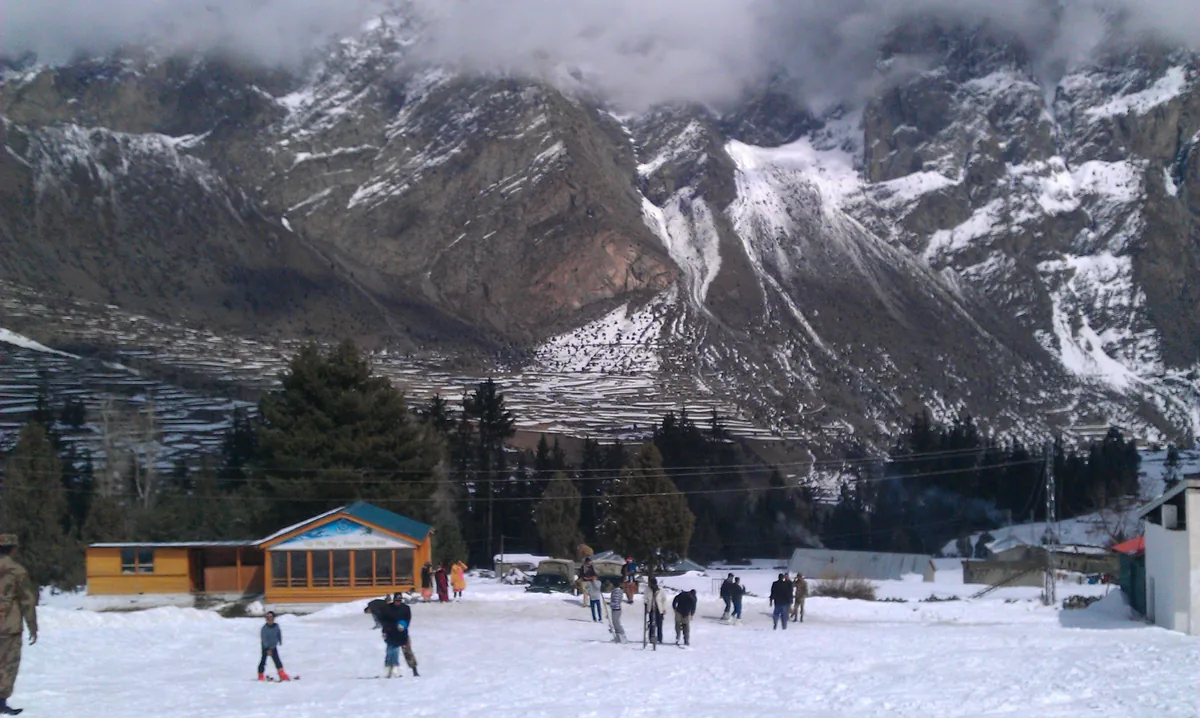 Skifahrer im Schnee des Skigebiets Naltar nahe Gilgit, mit der Lodge und verschneiten Gipfeln dahinter