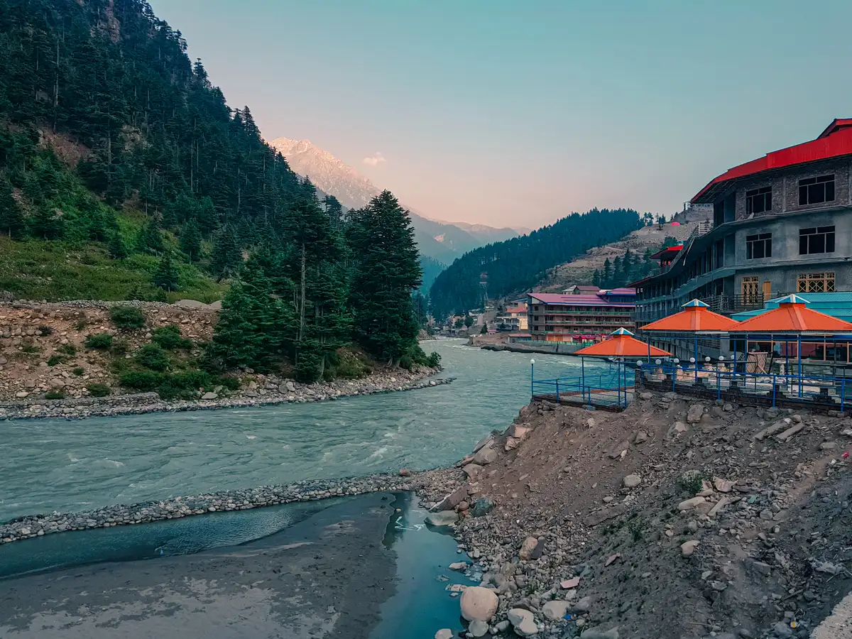 Alberghi con ombrelloni arancioni lungo il fiume Swat a Kalam, circondati da pinete e da una cima innevata, Khyber Pakhtunkhwa, Pakistan