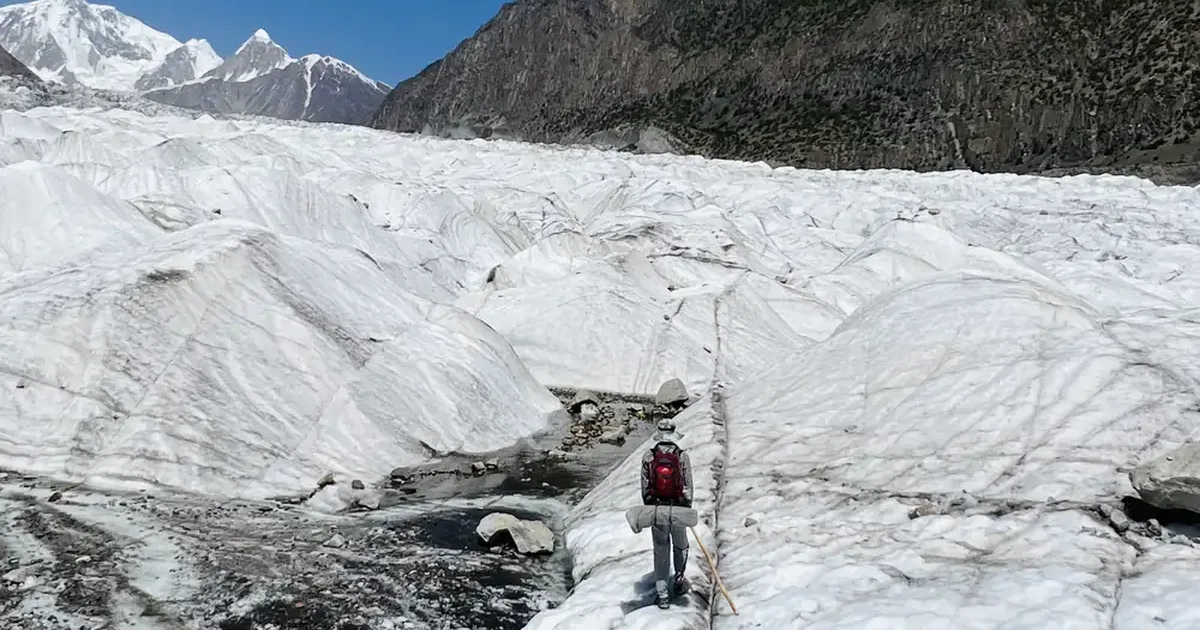 A trekker with a red backpack crossing the white ice of the Passu Glacier on the Patundas Meadows trek, Gojal, Upper Hunza, Pakistan