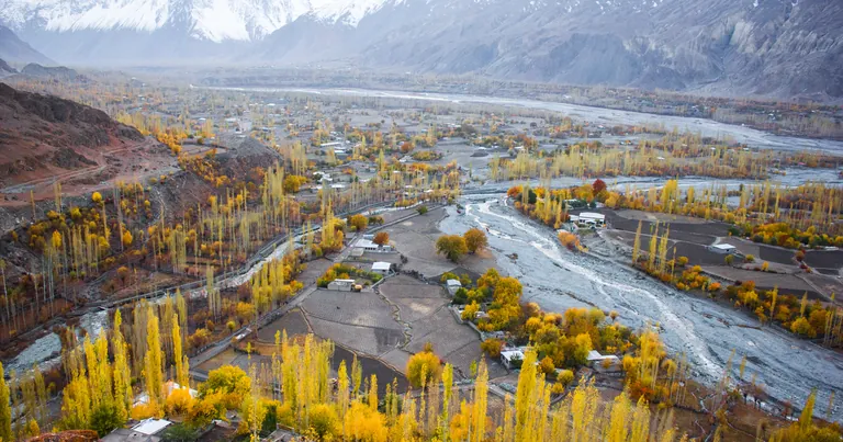 Aerial view of Sandhi village in Yasin Valley in autumn, golden poplars, fields and the braided Yasin River below snow-capped Hindu Kush mountains, Gilgit-Baltistan, Pakistan