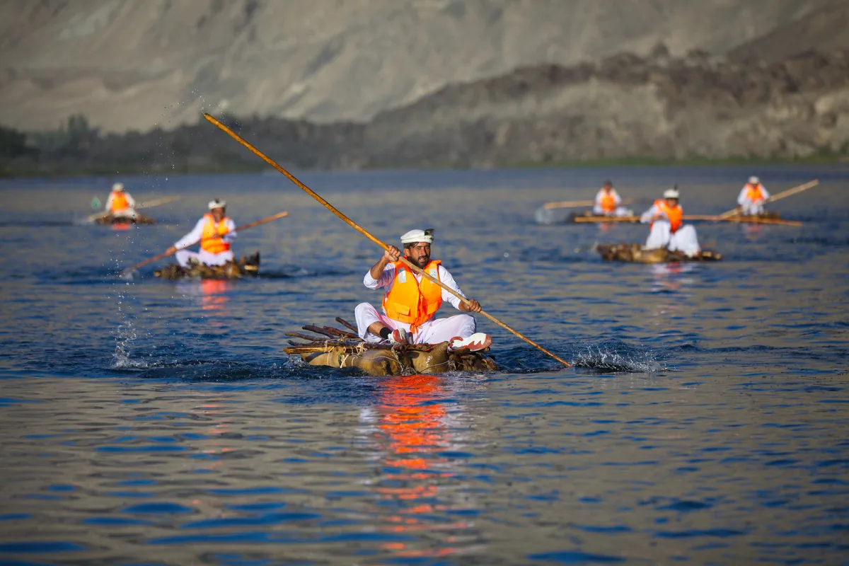 Bootsleute in Schwimmwesten paddeln traditionelle Zakh-Flöße bei einem Rennen auf dem Fluss bei Skardu, Baltistan