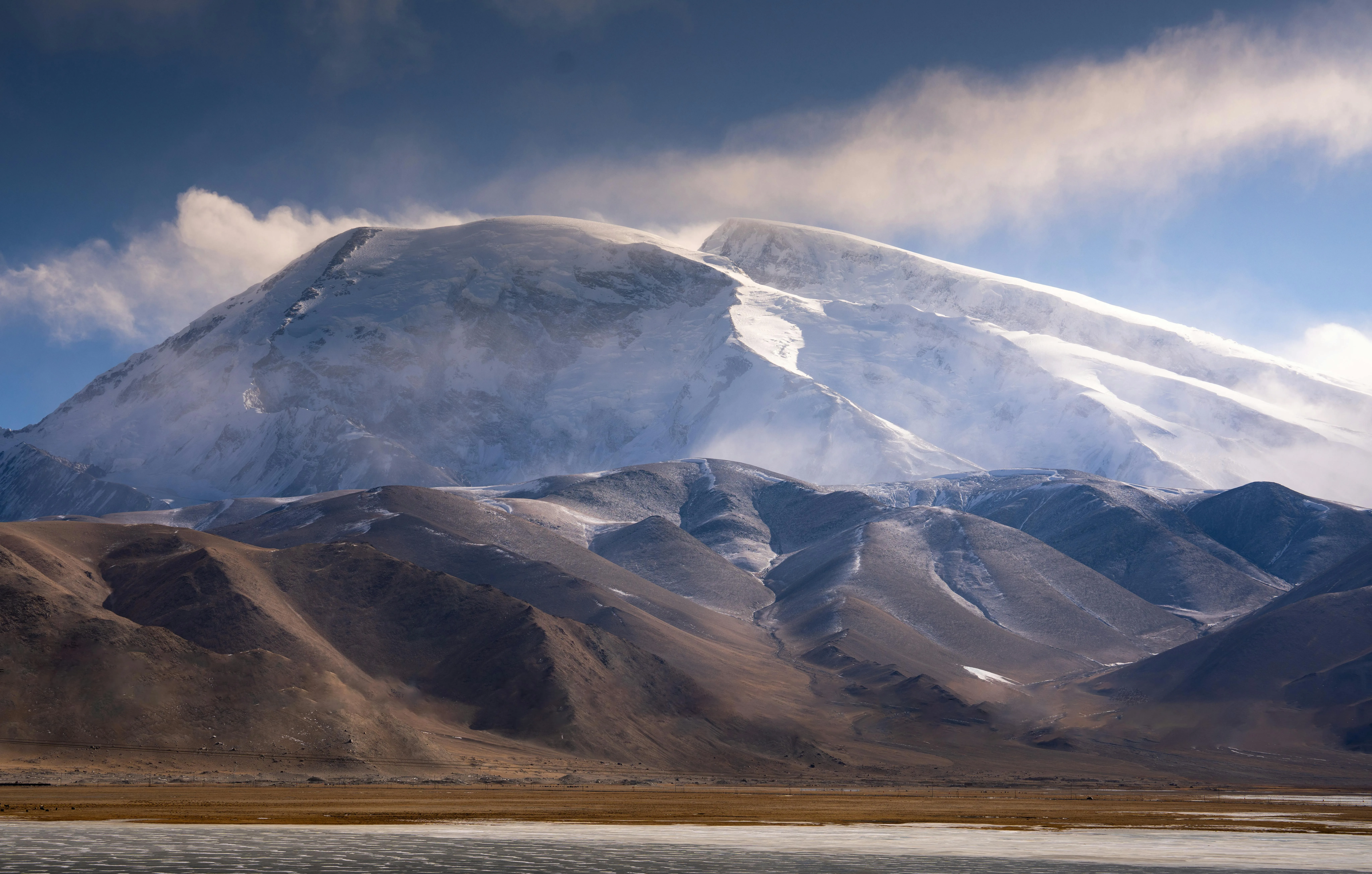 Muztagh Ata summit shrouded in mist with brown foothills