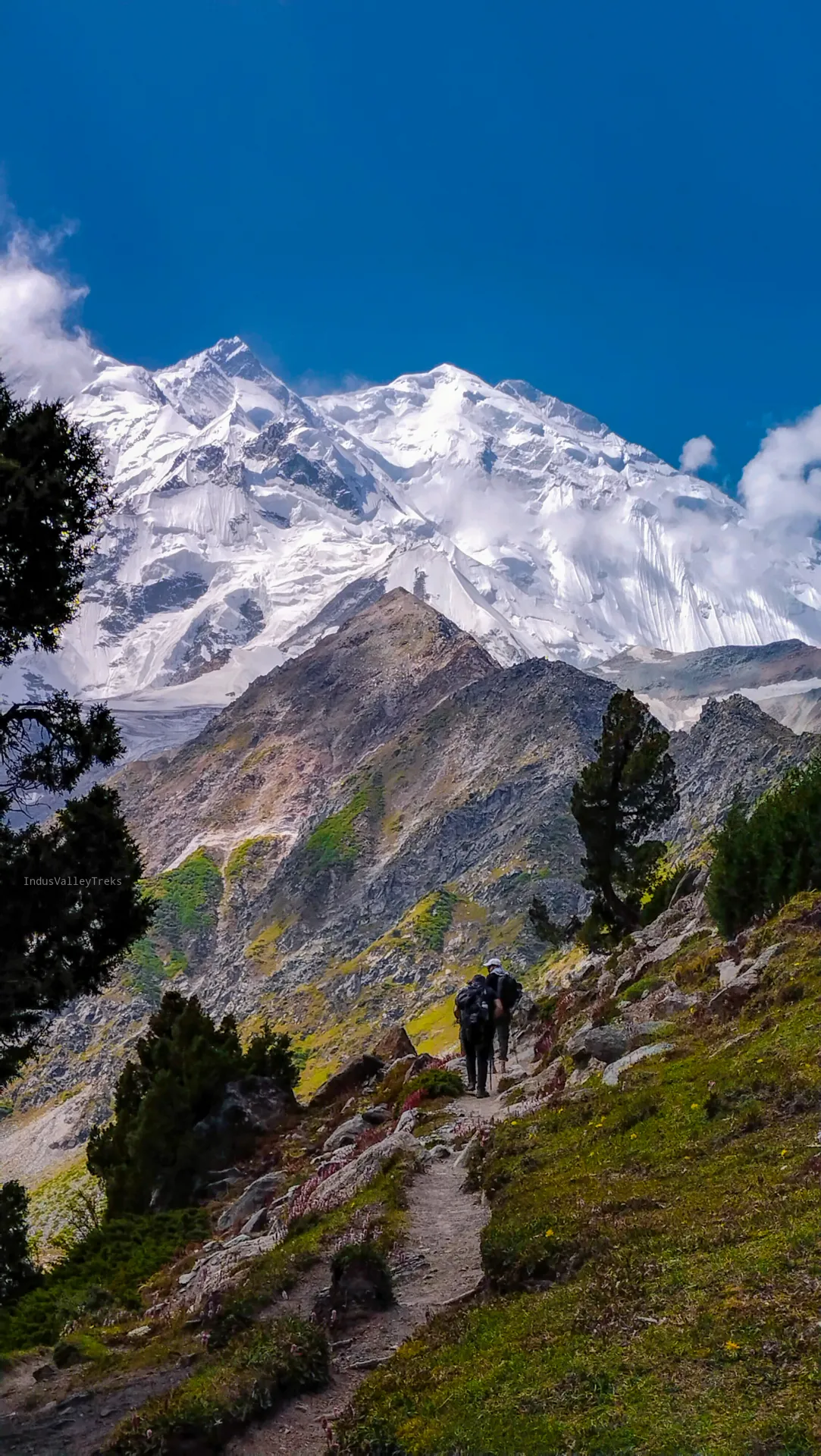 Two trekkers climbing toward the Raikot face of Nanga Parbat above Fairy Meadows
