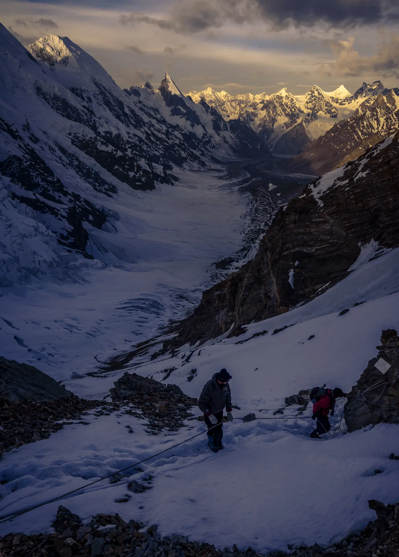 Climbers on fixed rope above the Gondogoro glacier at dawn, with Laila Peak and the Hushe peaks beyond
