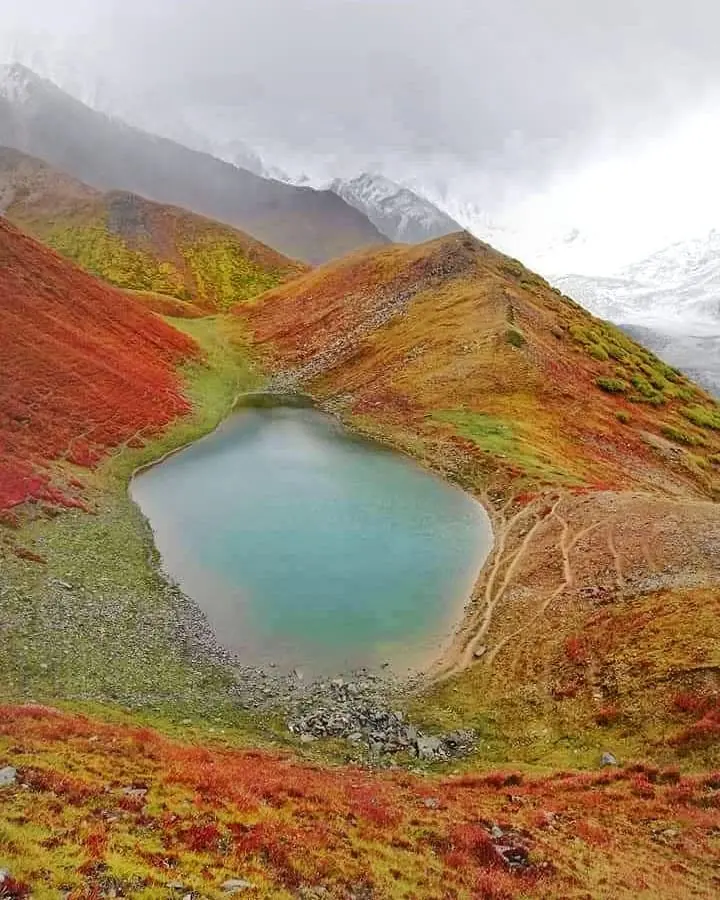 Kacheli Lake seen from the slope above, a turquoise tarn ringed by red autumn ground