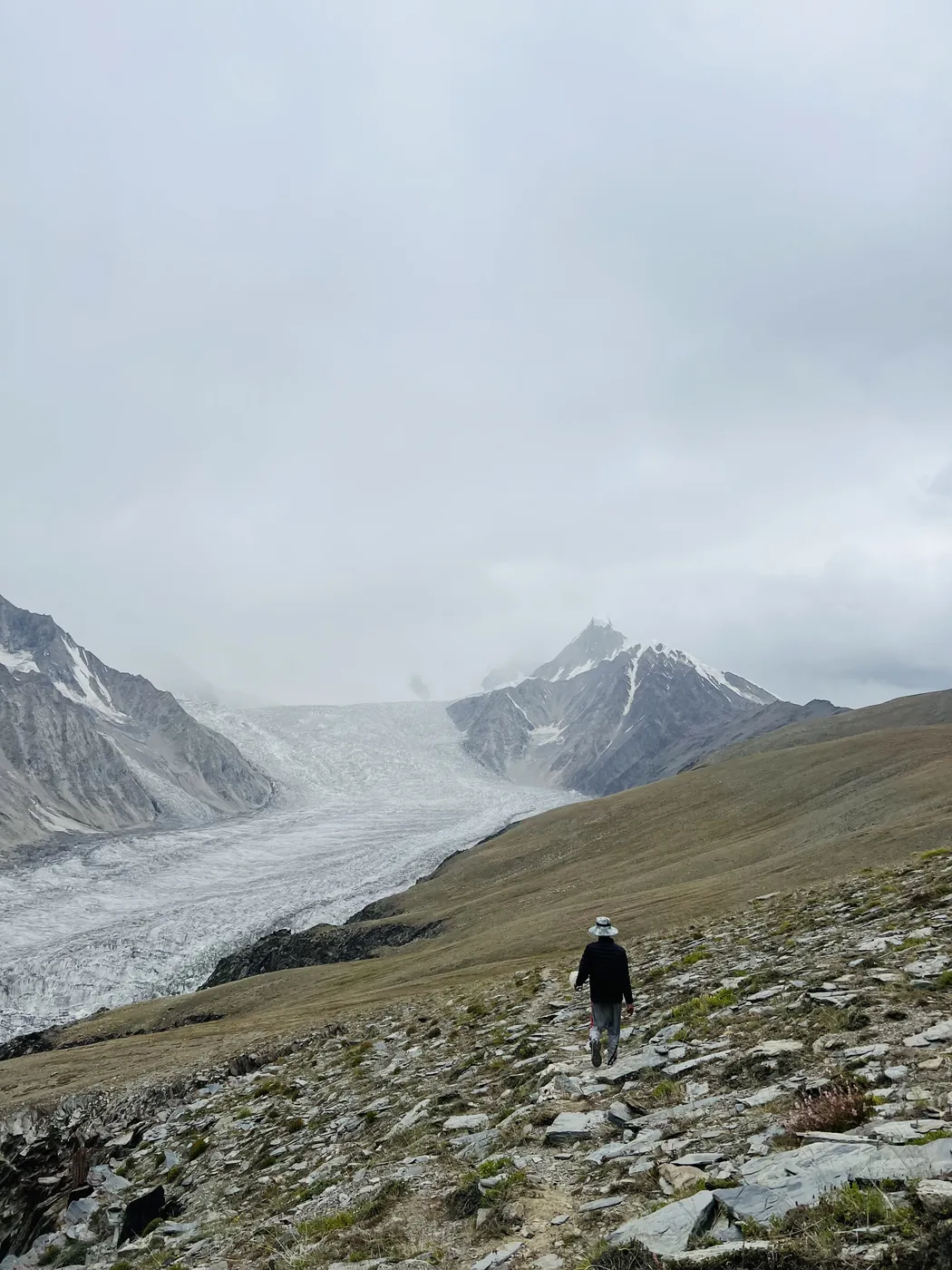 A trekker climbing the grassy ridge above the Passu Glacier in low cloud on the way to Patundas