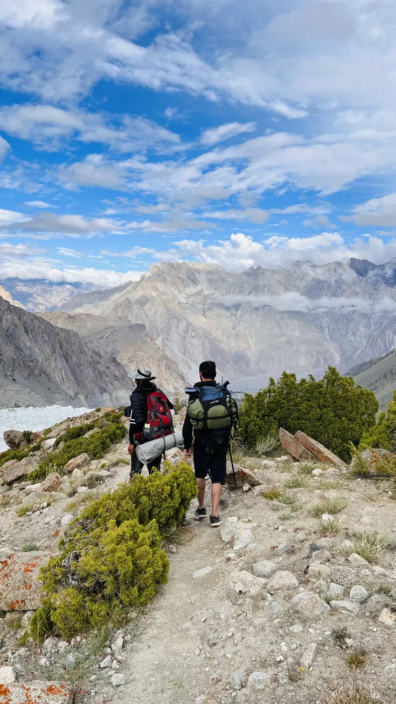 Two trekkers descending the juniper-lined trail from Patundas towards Borith Lake, Gojal