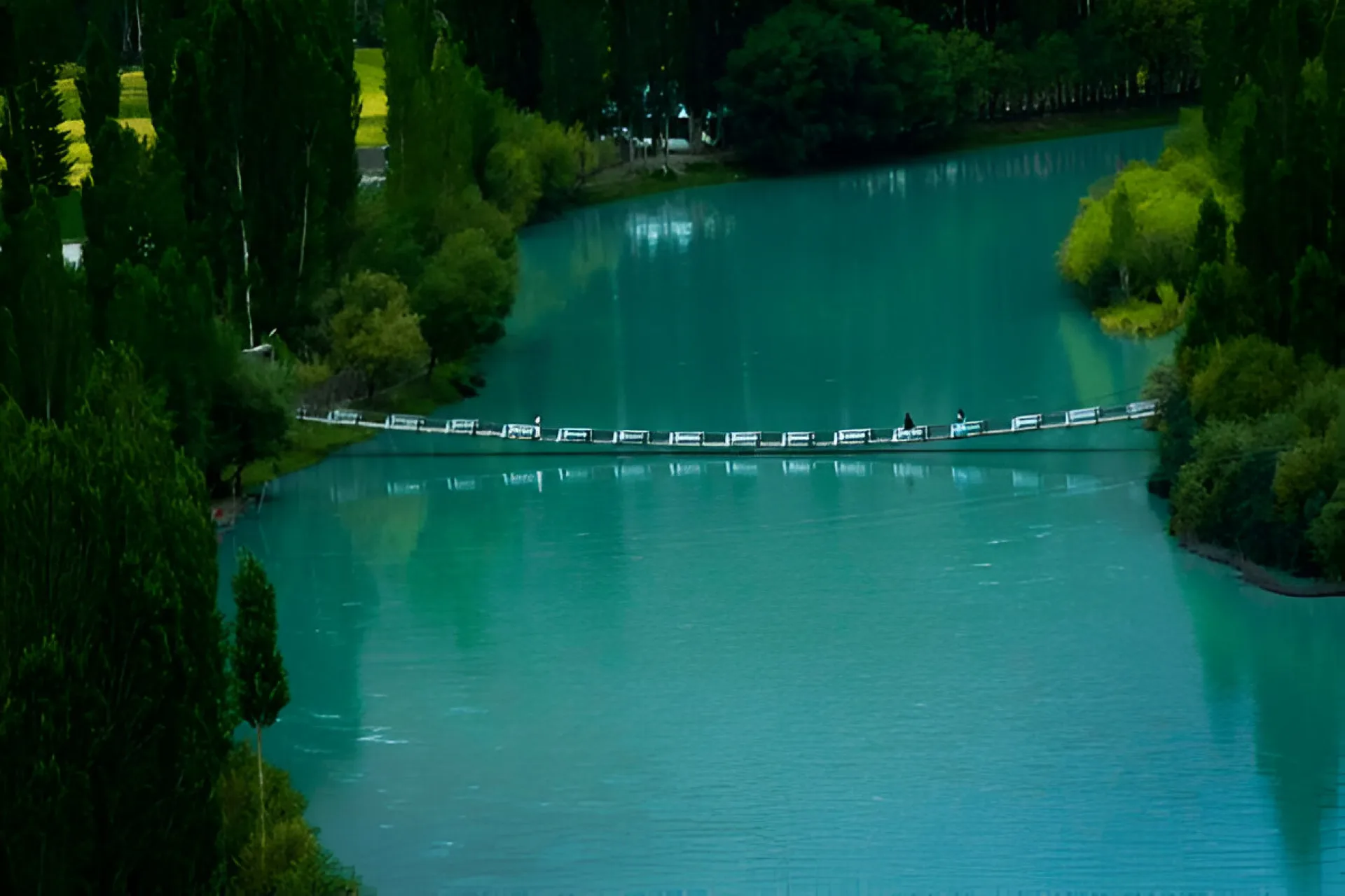 A narrow suspension bridge crossing the turquoise water of Phandar Lake in the Ghizer Valley