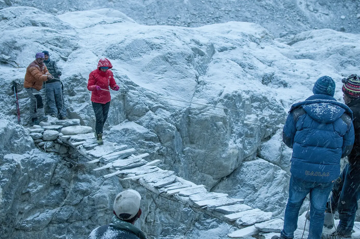 Einheimische halten Seile, während ein Trekker eine provisorische Brücke am Malangoti-Gletscher überquert
