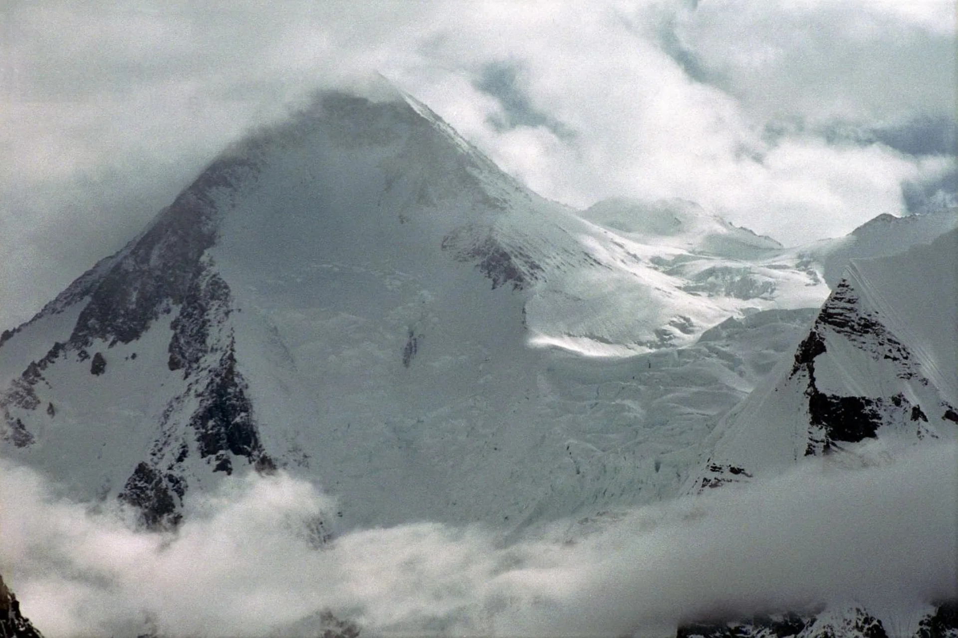 Gasherbrum I and Gasherbrum South peaks shrouded in clouds with glacier and rocky ridges