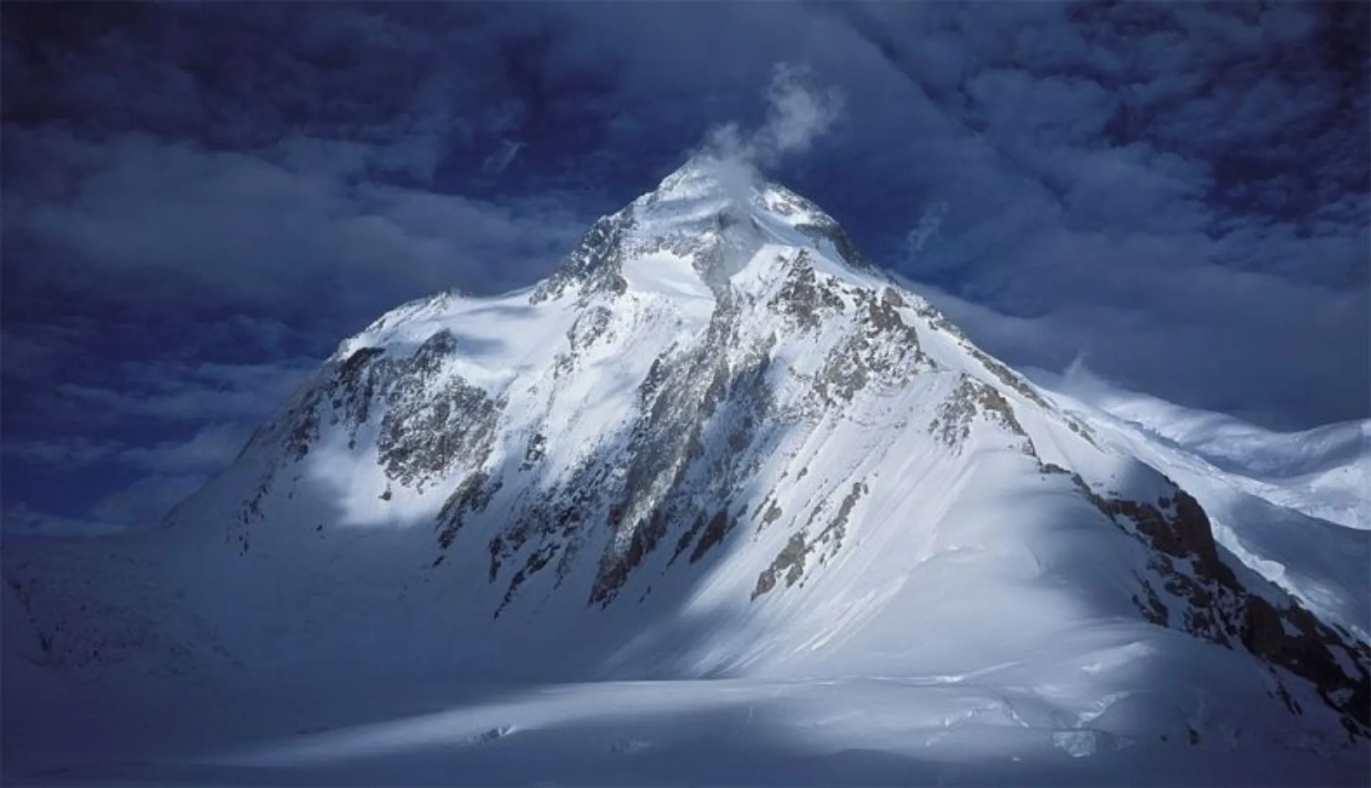 Gasherbrum I Hidden Peak 8080m summit pyramid with wind-blown snow against dark blue sky, Karakoram Pakistan
